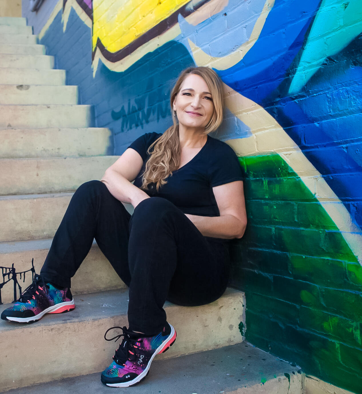 Helen Ryan sitting on stairs outdoors in front of graffiti wall
